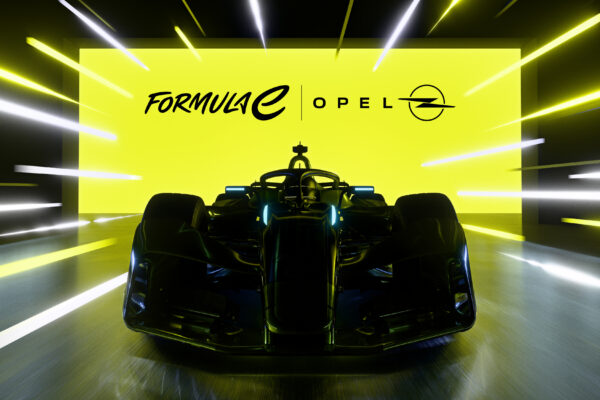 Frontansicht des Opel Formula E Gen4-Rennwagens in dunkler Lackierung, im Hintergrund eine leuchtend gelbe Wand mit den Logos von Formula E und Opel