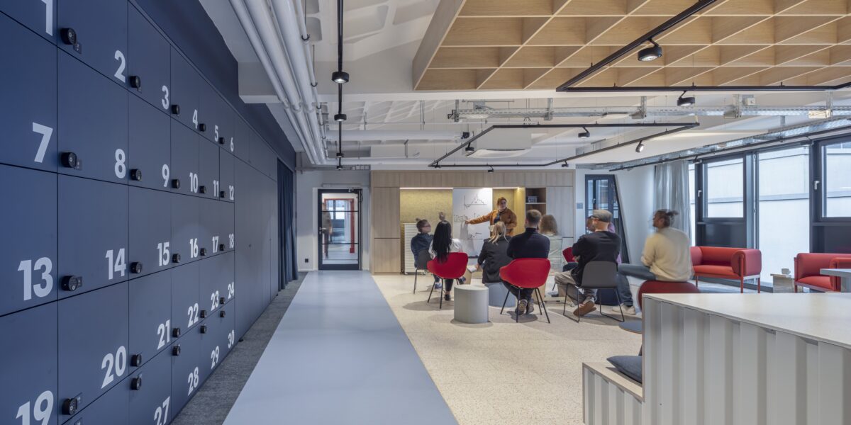 Offenes Büro mit blauen Schließfächern, roten Stühlen und Gruppe bei Whiteboard-Präsentation