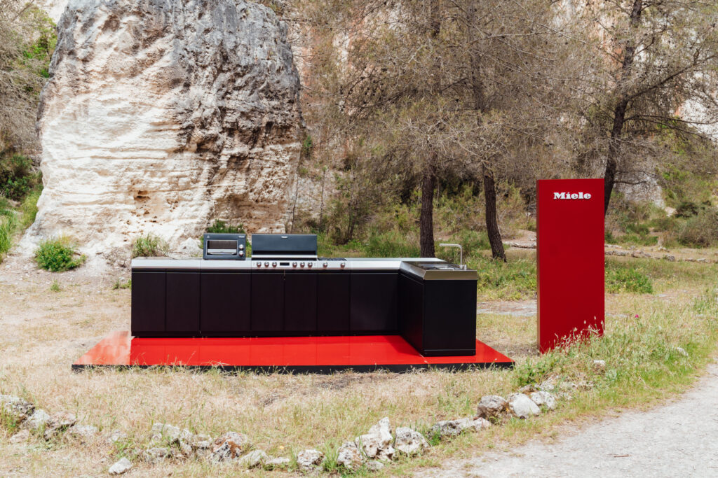 Miele Outdoor-Küche Dreams in schwarzem L-Design auf rotem Podest, aufgestellt in felsiger Naturlandschaft