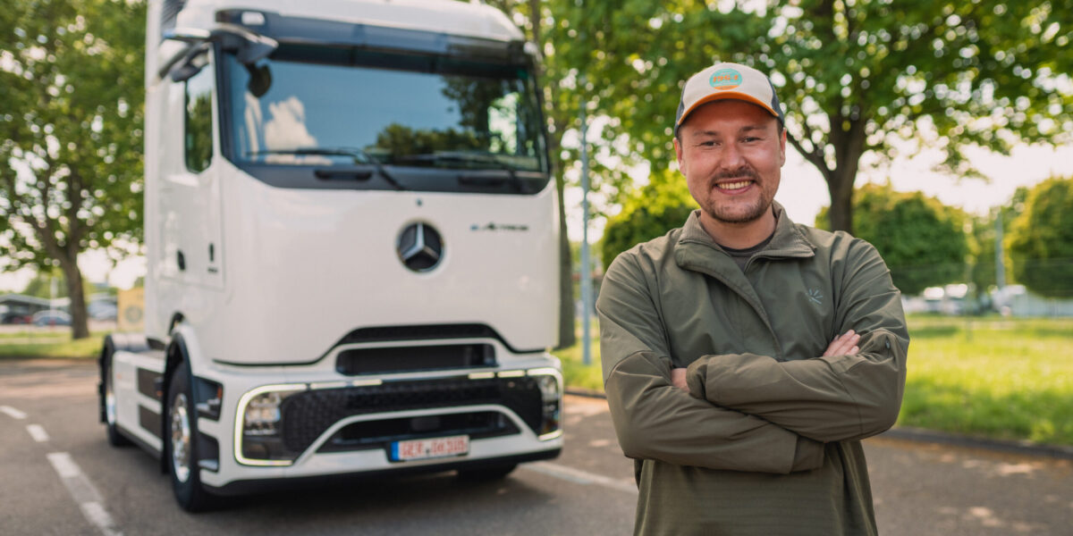 Mann mit Cap steht lächelnd vor weißem Mercedes-Benz eActros Elektro-LKW auf Parkplatz