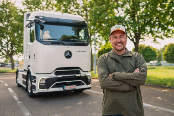 Mann mit Cap steht lächelnd vor weißem Mercedes-Benz eActros Elektro-LKW auf Parkplatz