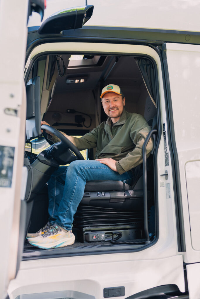 Lächelnder Lkw-Fahrer sitzt im Fahrerhaus eines weißen Lkw, Hand am Lenkrad