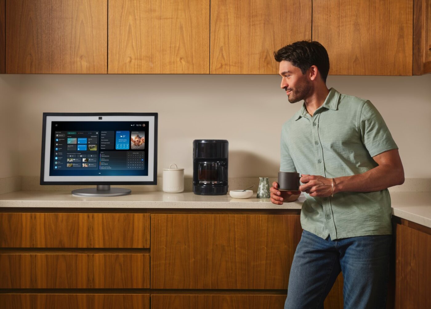 Mann in Küche blickt auf Amazon Echo Show mit Alexa+-Dashboard, Kaffeetasse in der Hand
