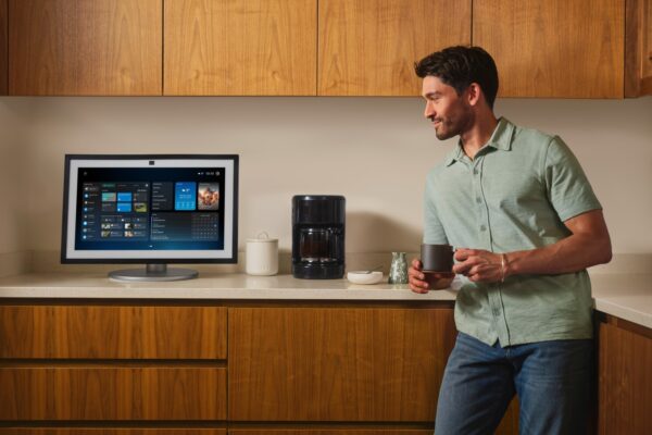 Mann in Küche blickt auf Amazon Echo Show mit Alexa+-Dashboard, Kaffeetasse in der Hand