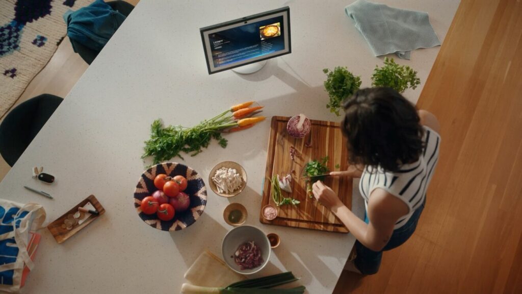 Frau schneidet Gemüse in der Küche, Amazon Echo Show zeigt Lasagne-Rezept via Alexa+