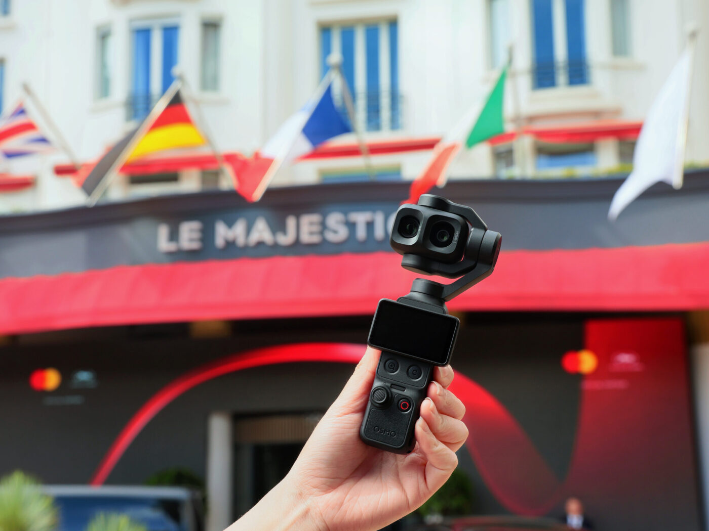 Hand hält DJI Osmo Pocket 4P mit Dual-Objektiv vor dem Hotel Le Majestic in Cannes