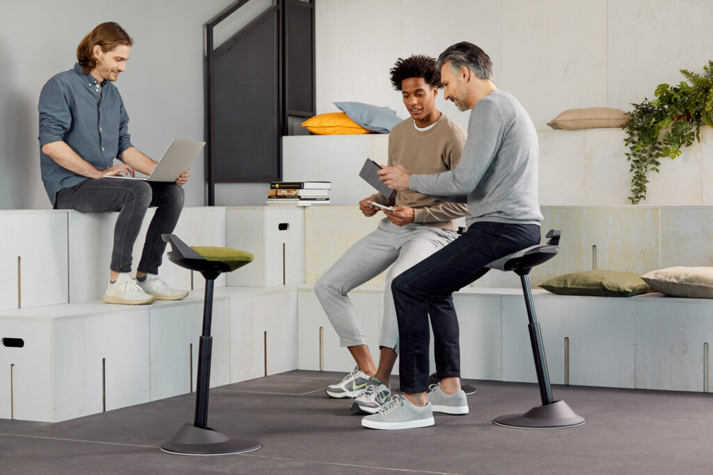 Zwei Männer auf ergonomischen Aeris-Hockern im Büro-Lounge-Bereich schauen gemeinsam auf ein Tablet