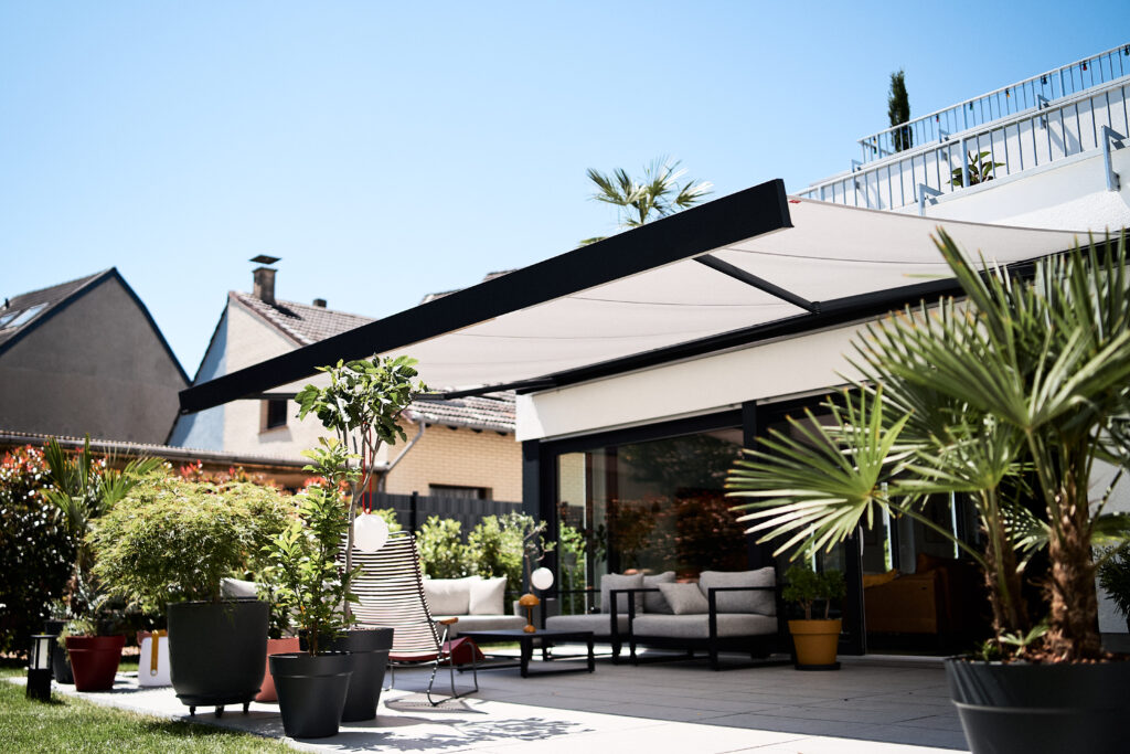 Automatische Markise über moderner Terrasse mit Outdoor-Lounge und Palmen an einem sonnigen Tag