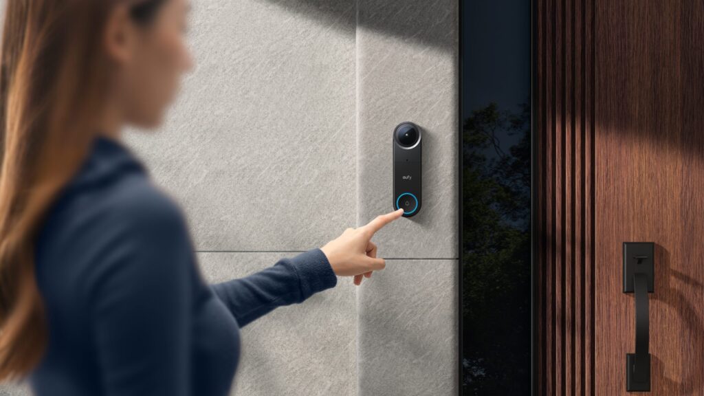 Frau drückt den Klingelknopf der eufy Video Doorbell S4 an grauer Steinwand neben Holzeingangstür