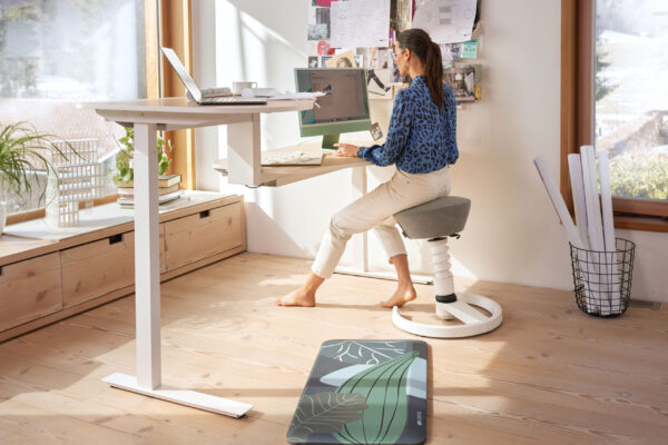 Frau arbeitet auf Aeris-Aktivhocker am höhenverstellbaren Schreibtisch im Home-Office