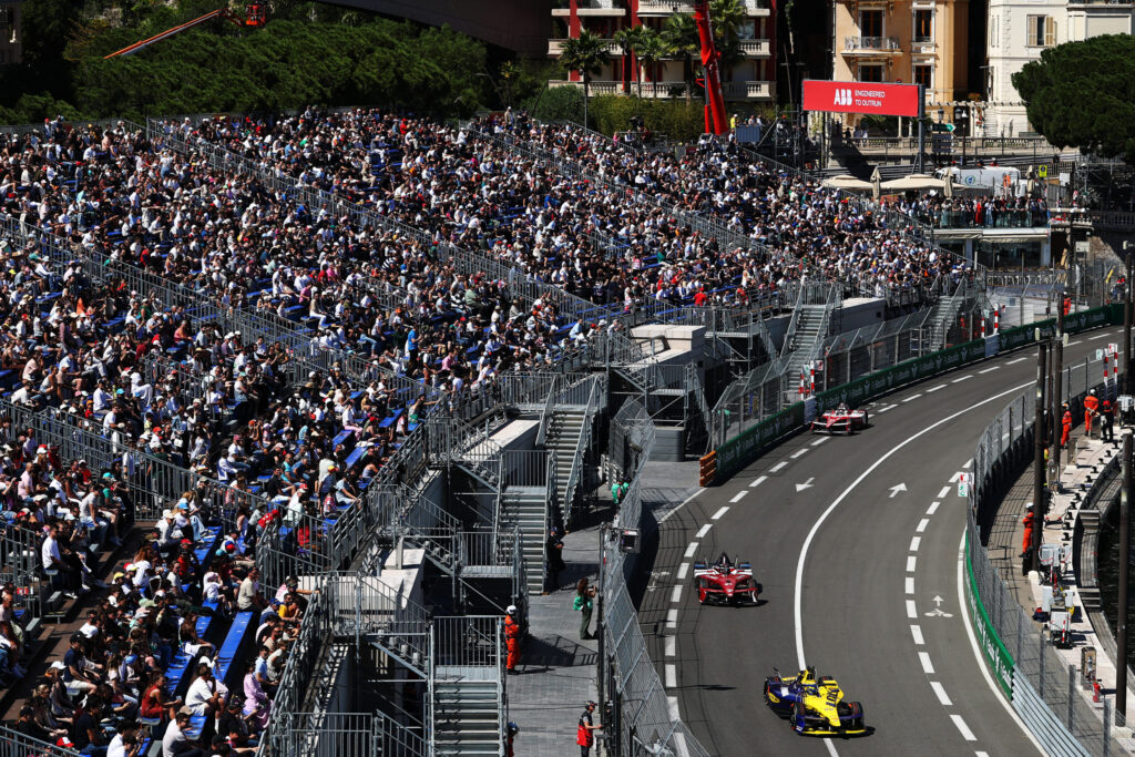Formula-E-Boliden beim Monaco E-Prix 2026 auf dem Stadtkurs, vollbesetzte Tribünen links