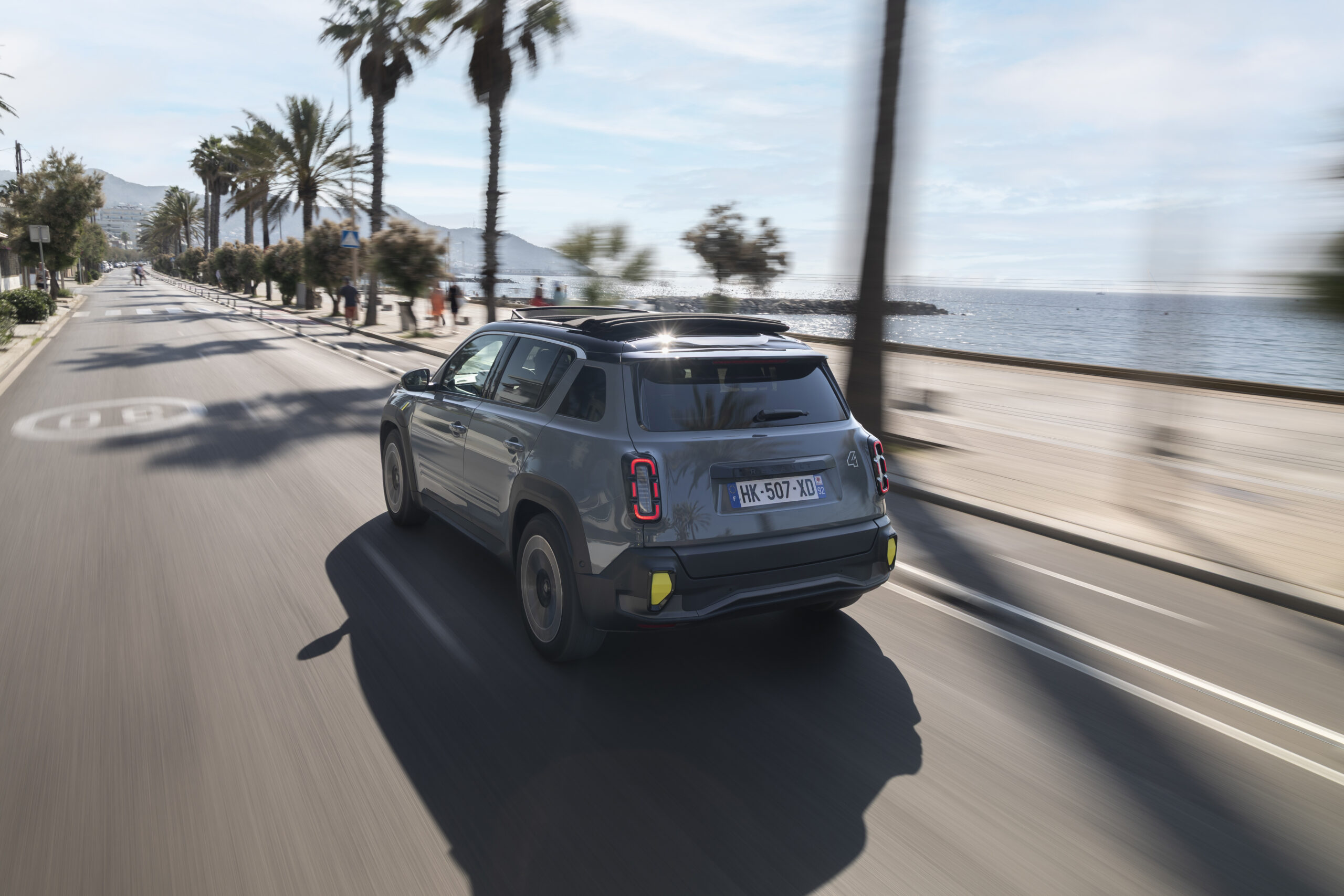 Renault 4 E-Tech Plein Sud in Grau von hinten auf Küstenstraße mit Palmen und Meer