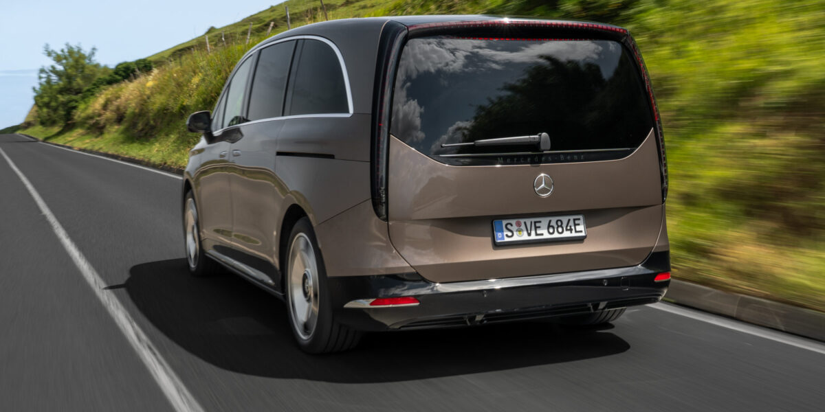 Mercedes-Benz VLE in Bronze-Metallic, Heckansicht auf Landstraße mit grüner Hügellandschaft