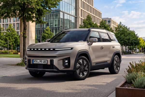 KGM Torres EVX Nomad in Champagner-Metallic vor modernem Stadtgebäude, Frontansicht schräg