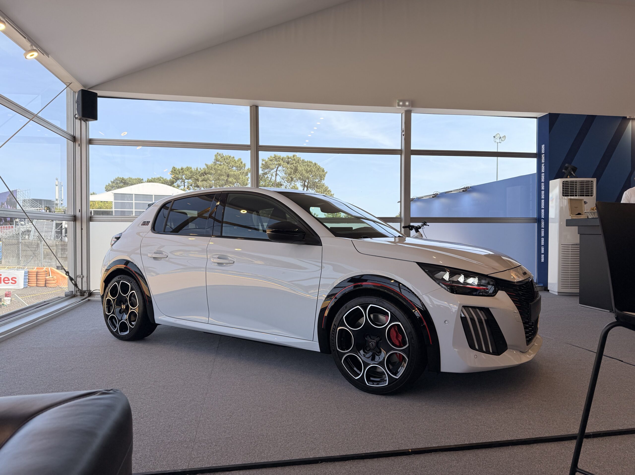 Peugeot E-208 GTi in Weiß im Ausstellungspavillon, Dreiviertelansicht mit roten Bremssätteln