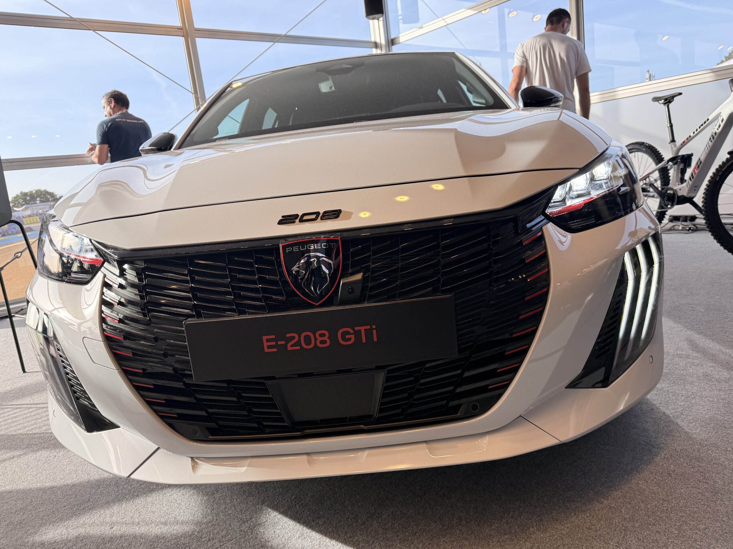 Peugeot E-208 GTi in Weiß, Frontansicht mit schwarzem Grill und roten Akzenten auf Ausstellung