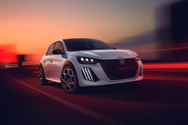 Peugeot E-208 GTi in Weiß fährt bei Sonnenuntergang auf einer Straße, Frontansicht