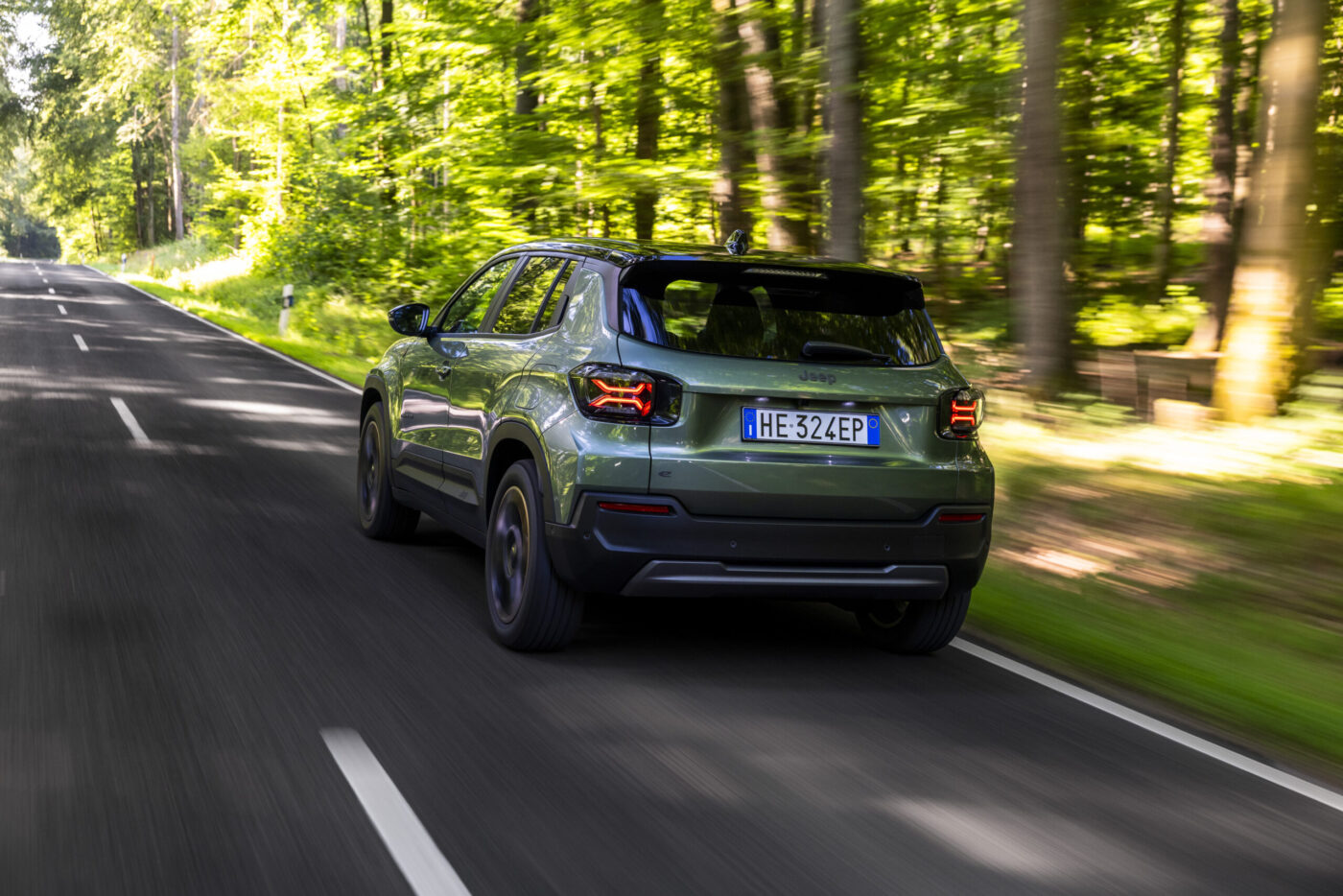 Jeep Avenger 2026 Facelift in Olivgrün, Heckansicht auf Waldstraße mit X-förmigen LED-Rückleuchten