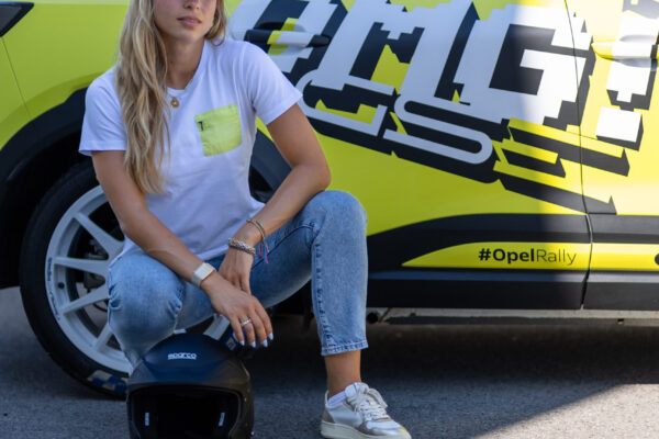 Sophia Flörsch hockt vor dem gelb-schwarzen Opel Mokka GSE Rally mit Sparco-Helm