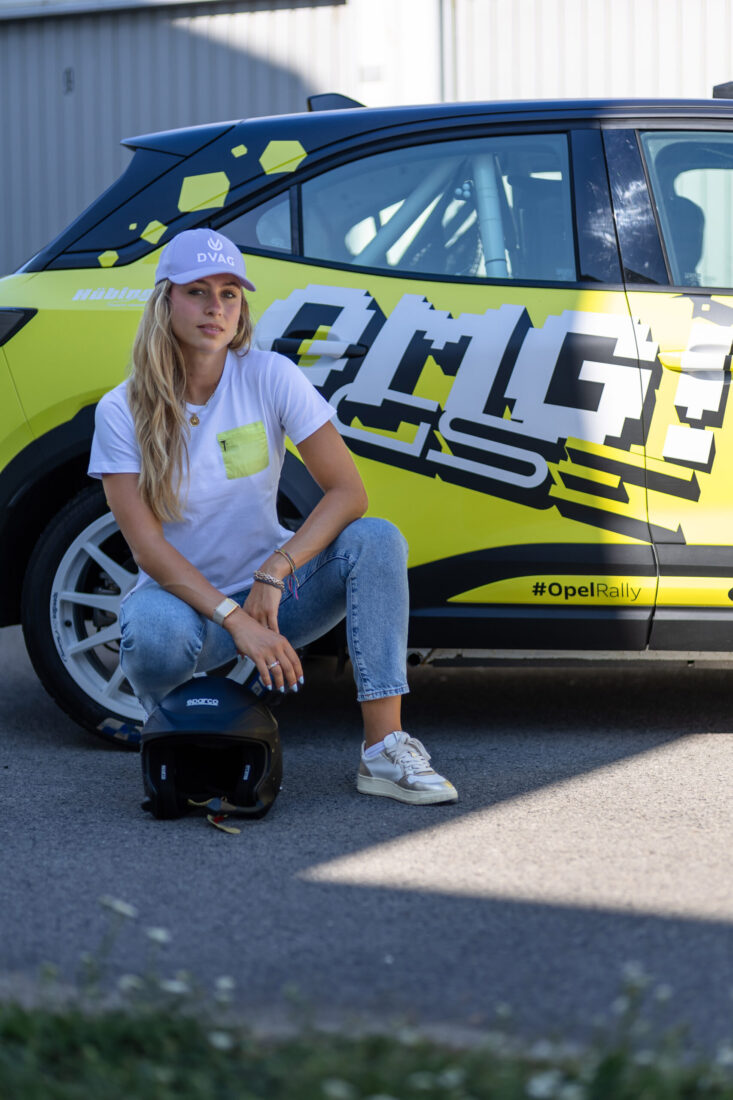Sophia Flörsch hockt vor dem gelb-schwarzen Opel Mokka GSE Rally mit Sparco-Helm