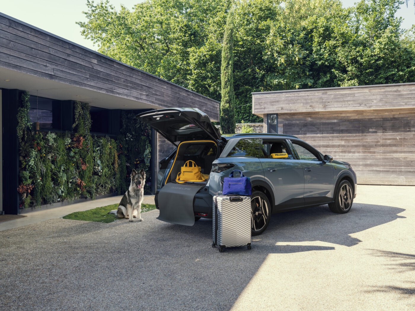 Peugeot E-5008 Dog Edition Concept mit offenem Kofferraum, Schäferhund und Reisegepäck vor modernem Haus