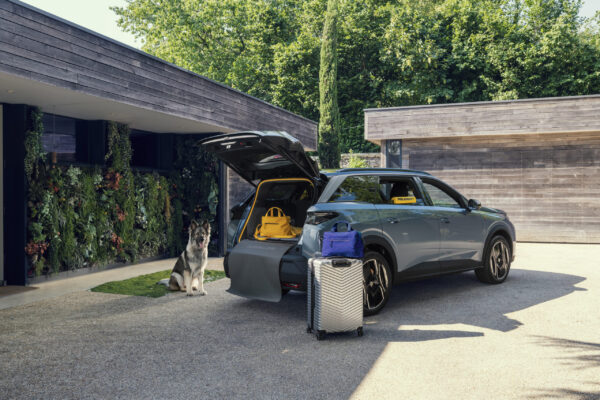 Peugeot E-5008 Dog Edition Concept mit offenem Kofferraum, Schäferhund und Reisegepäck vor modernem Haus
