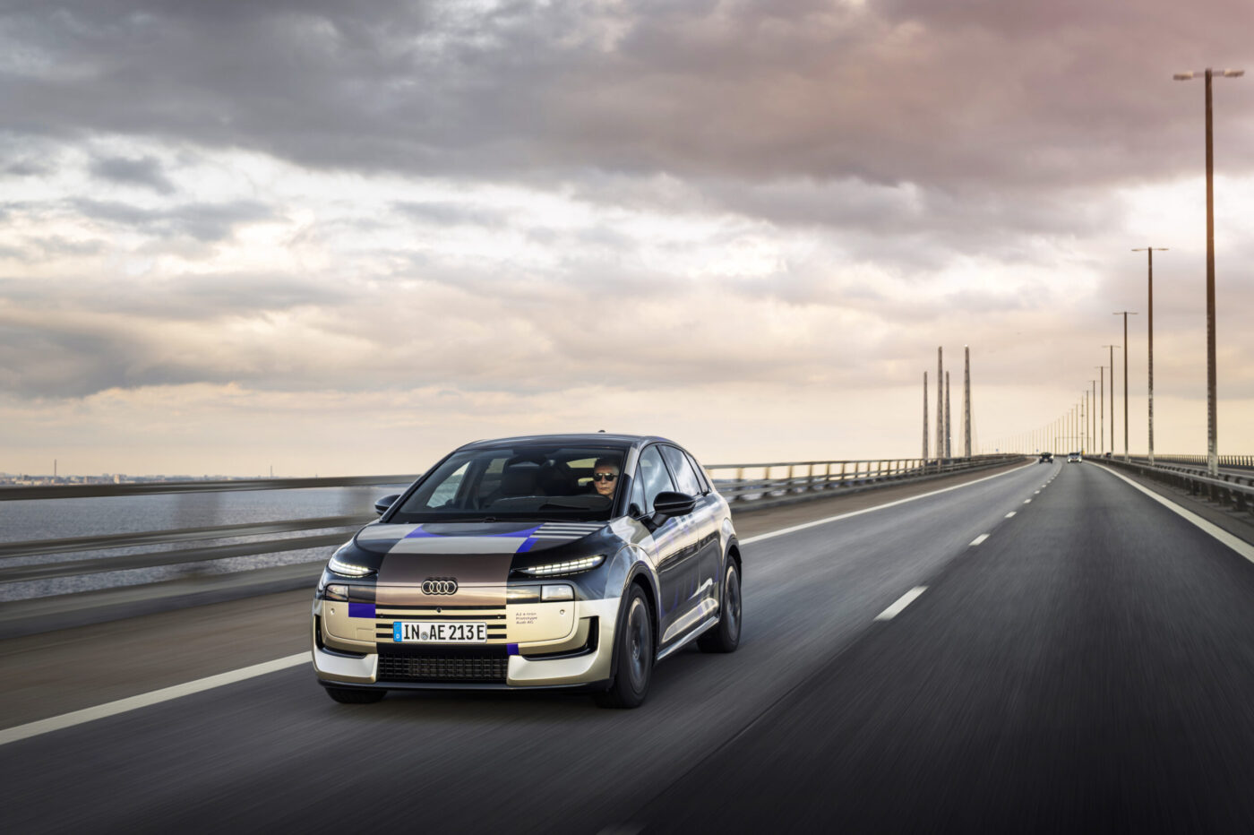 Audi A2 e-tron Prototyp mit Tarnfolie auf einer Brückenautobahn, Frontansicht in Fahrt