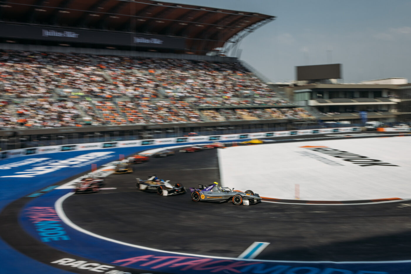 Formel-E-Rennautos in der Kurve eines Stadtkurses vor vollbesetzter Tribüne