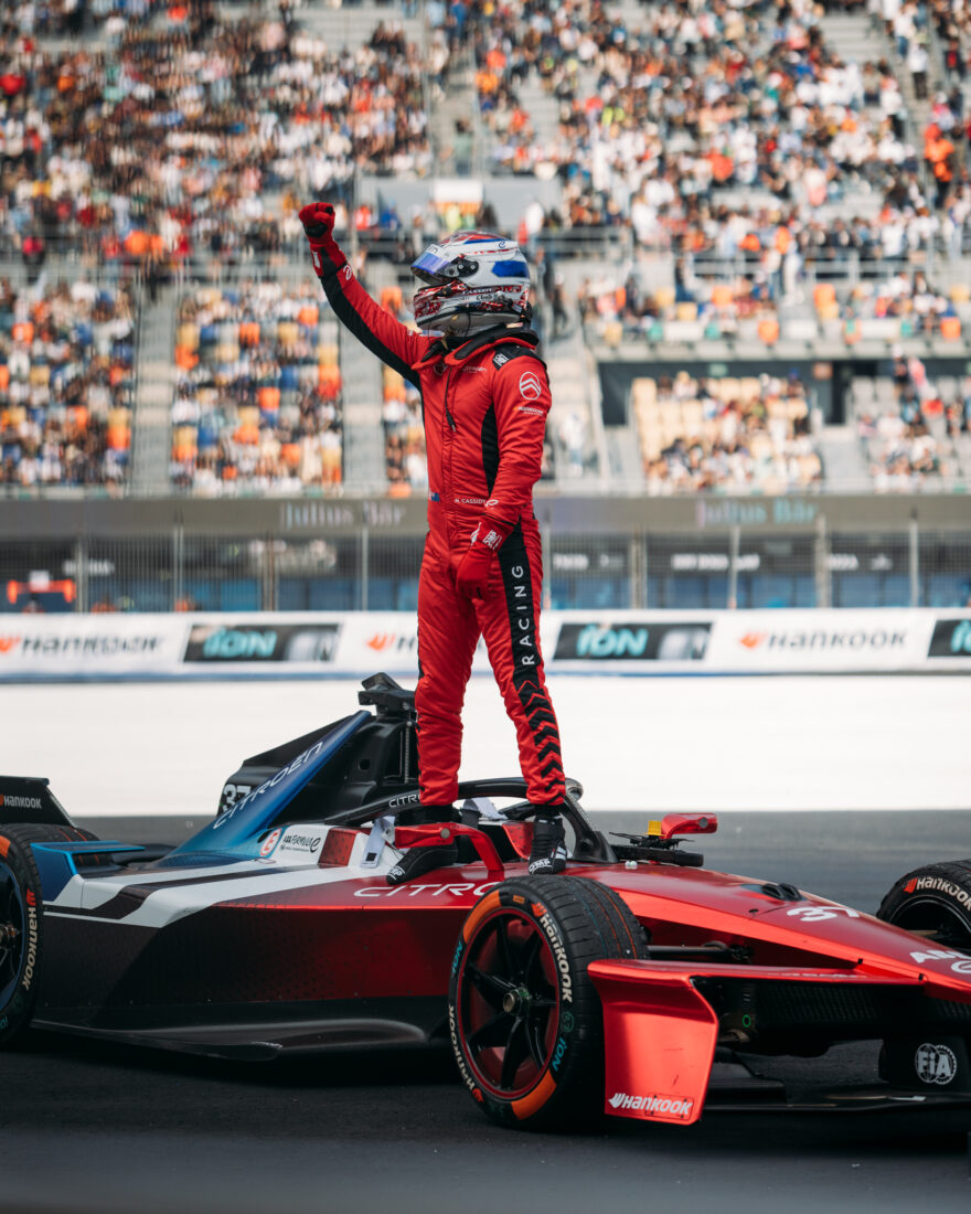 Citroën-Formel-E-Pilot steht siegesjubelnd mit erhobener Faust auf seinem roten GEN3-Boliden vor vollen Tribünen