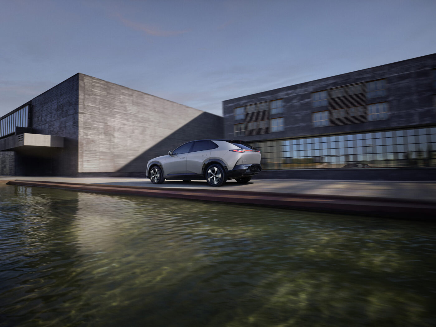 Mazda CX-6e in Silber fährt an einem modernen Betongebäude entlang einem Wasserbecken