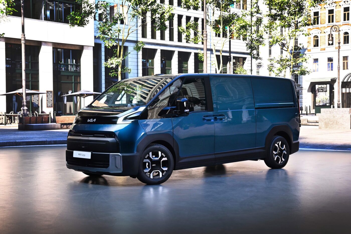 Kia PV7 Cargo in Blaugrün, Frontansicht schräg links, vor urbaner Kulisse
