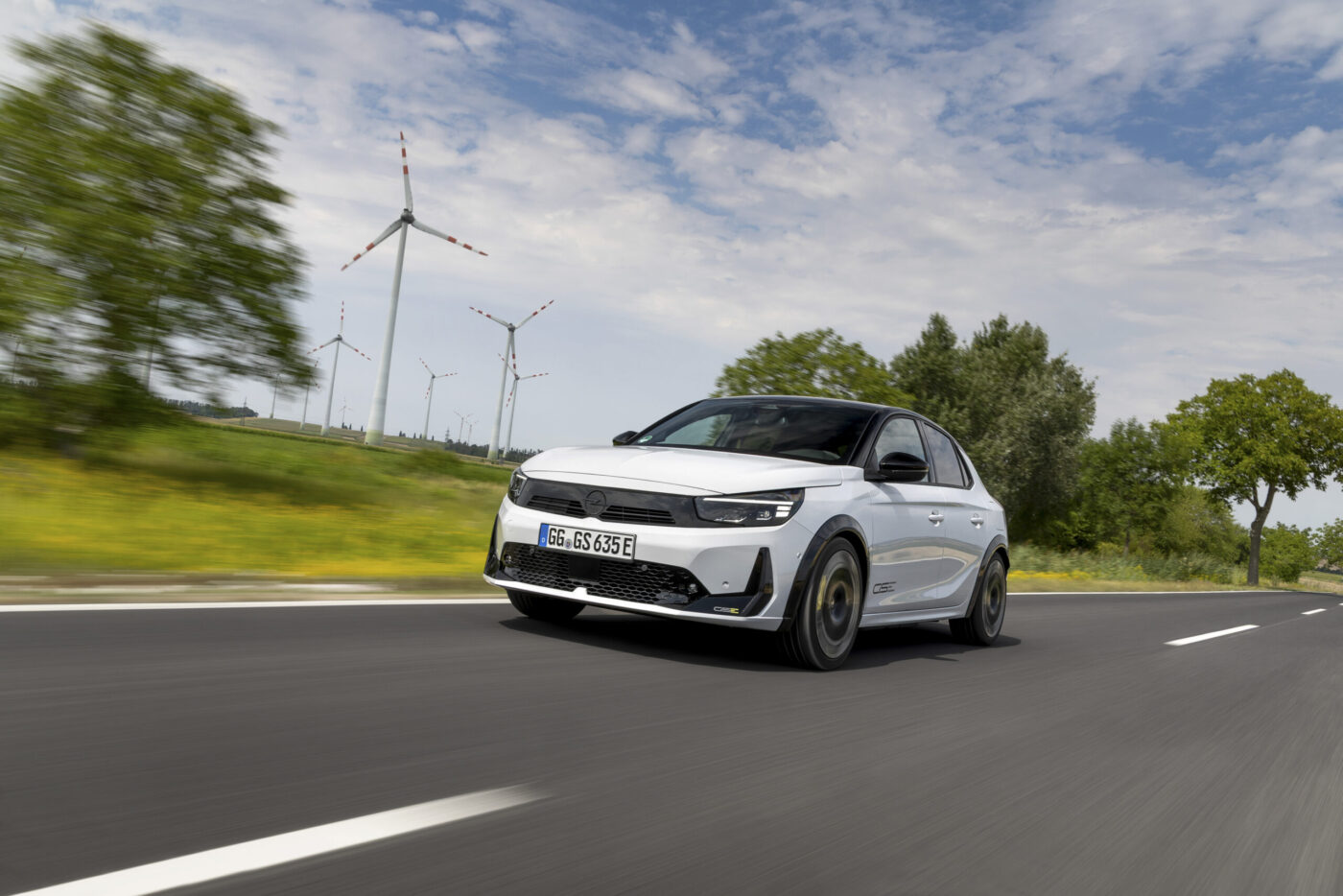 Opel Corsa GSE Electric in Weiß, fahrend auf Landstraße mit Windrädern im Hintergrund