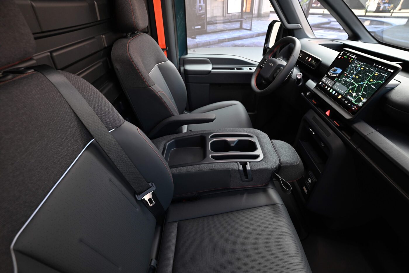 Kia PV7 Cockpit mit großem Touchscreen-Display, dunkelgrauen Sitzen mit roten Ziernähten und Mittelkonsole