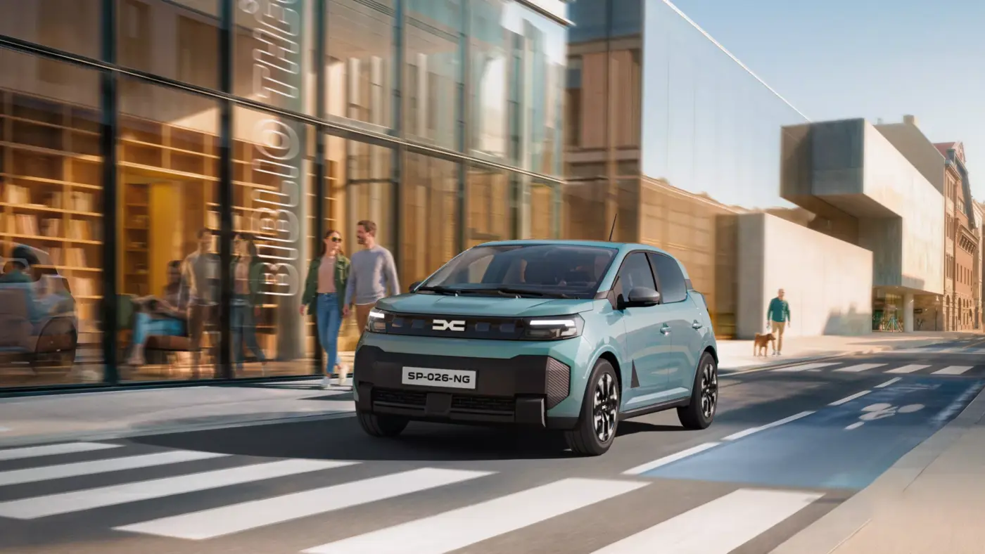 Dacia Spring 2. Generation in Türkis fährt durch eine Stadtstraße mit Fußgängern
