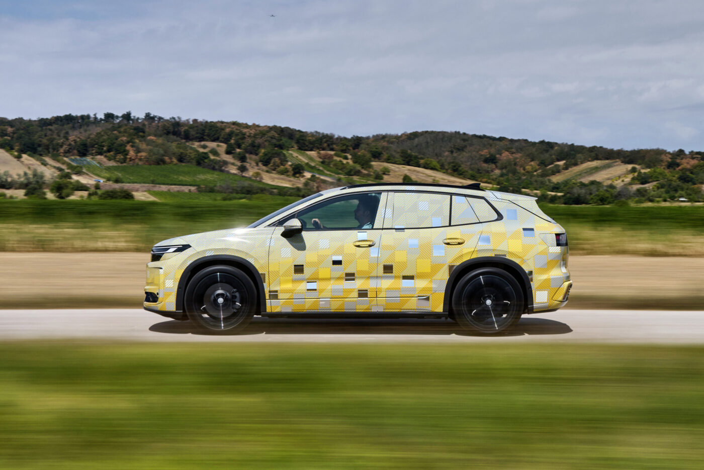 VW ID. Tiguan Prototyp mit gelbem Pixel-Tarnmuster in Fahrt auf Landstraße