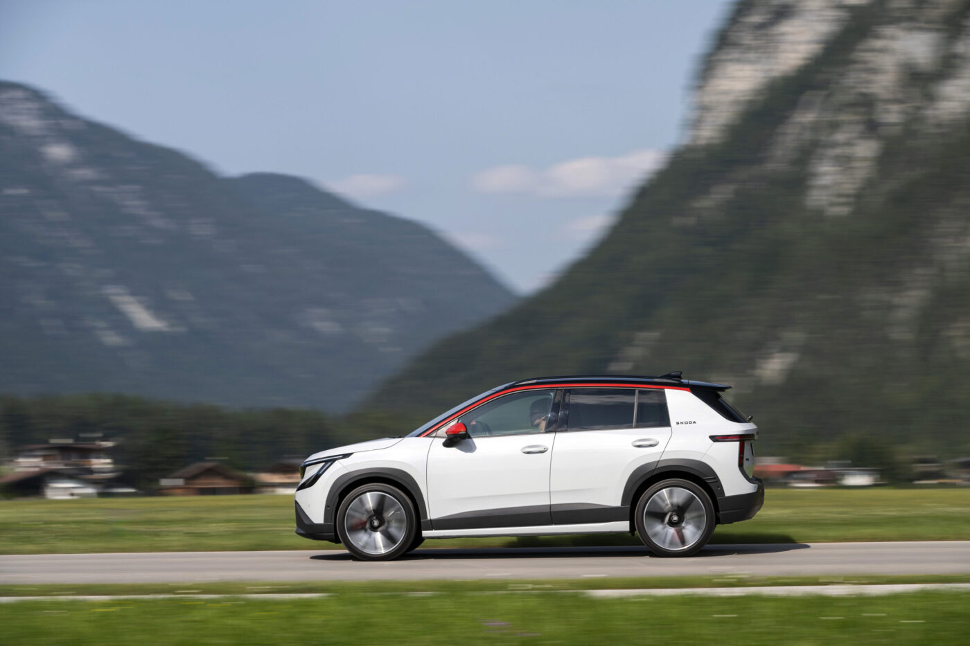 Škoda Epiq in Weiß mit rotem Dachrahmen fährt auf einer Straße vor Alpenkulisse