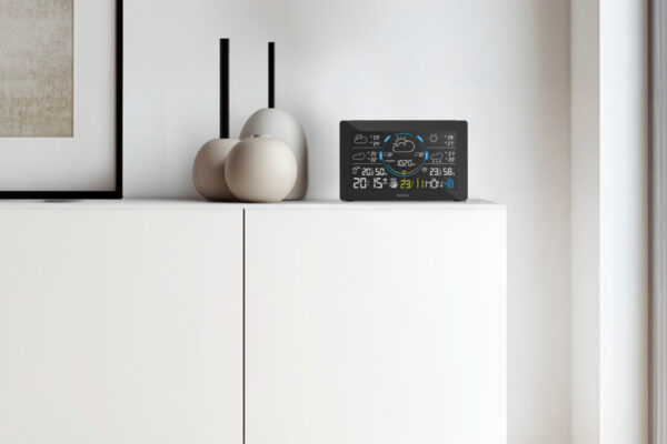 Hama WLAN-Wetterstation mit Farbdisplay auf weißem Sideboard, zeigt Uhrzeit, Temperatur und Wettervorhersage