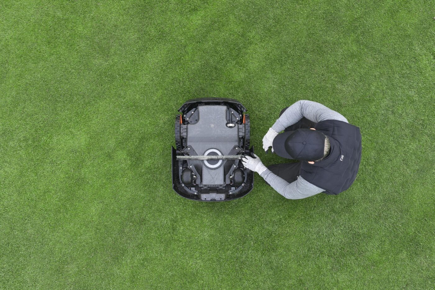 Person untersucht von oben die Unterseite eines Husqvarna Automower 580L EPOS auf Golfrasen