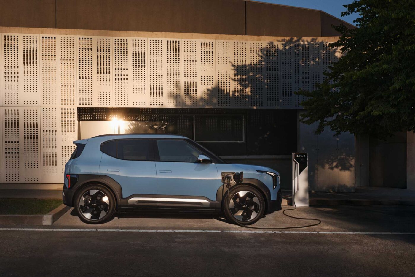 Kia EV3 in Hellblau lädt an einer Kia-AC-Ladestation vor moderner Gebäudefassade