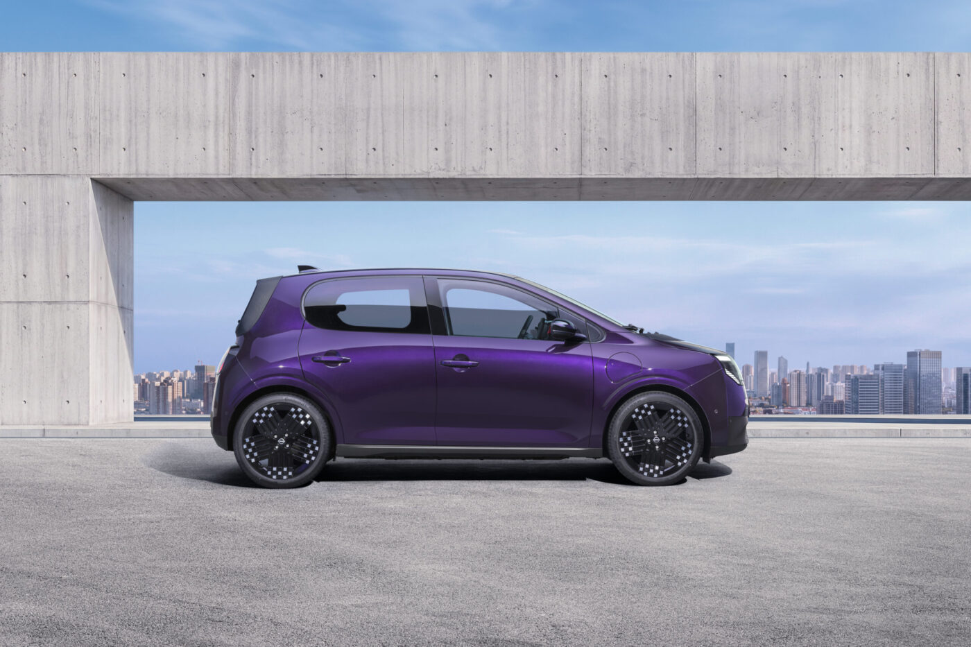 Nissan Pixo Elektro in Violett, Seitenansicht vor Betonarchitektur und Stadtpanorama