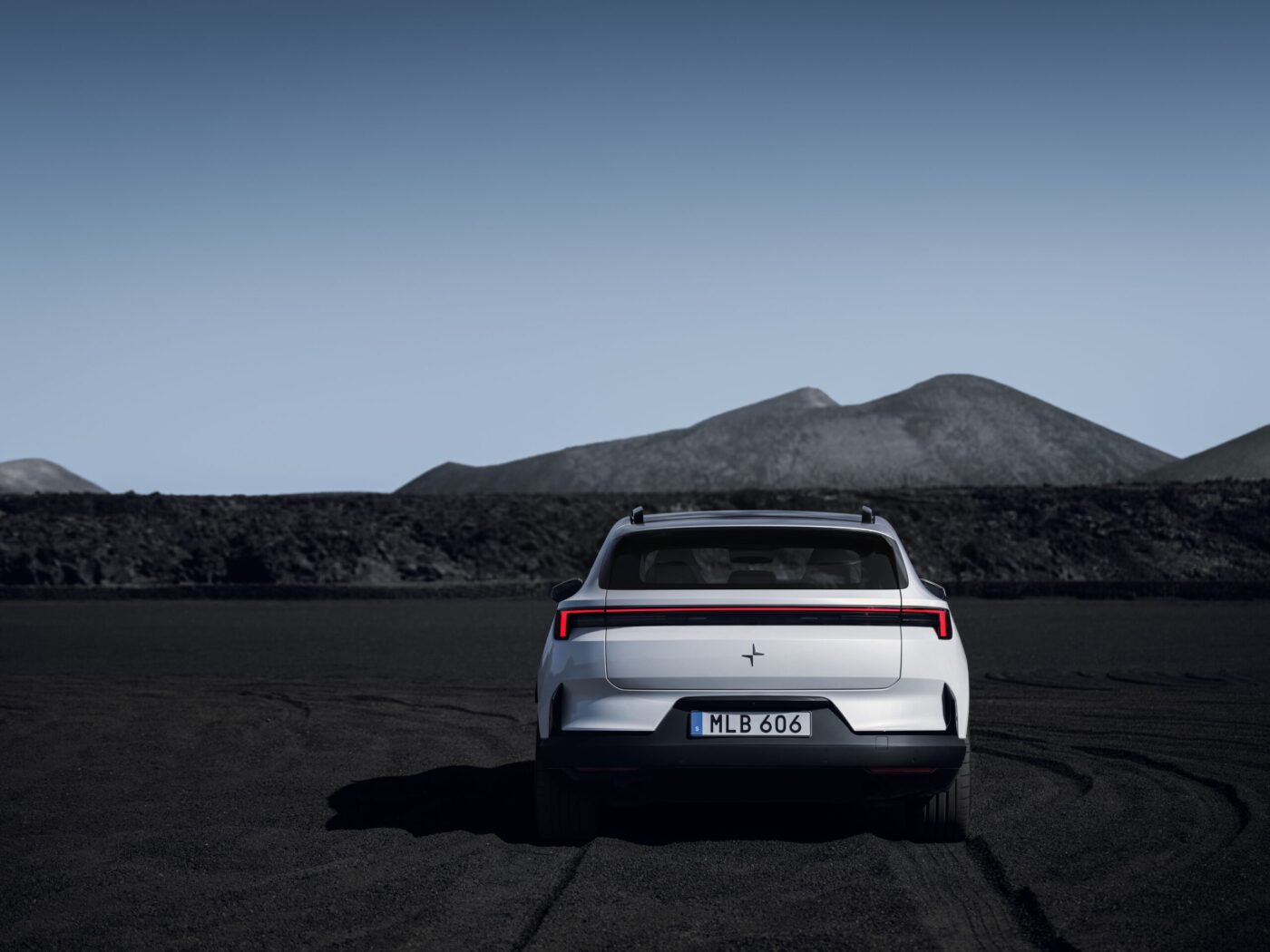Polestar 4 SUV in Weiß, Heckansicht mit durchgehendem roten Leuchtband, vor Vulkanlandschaft