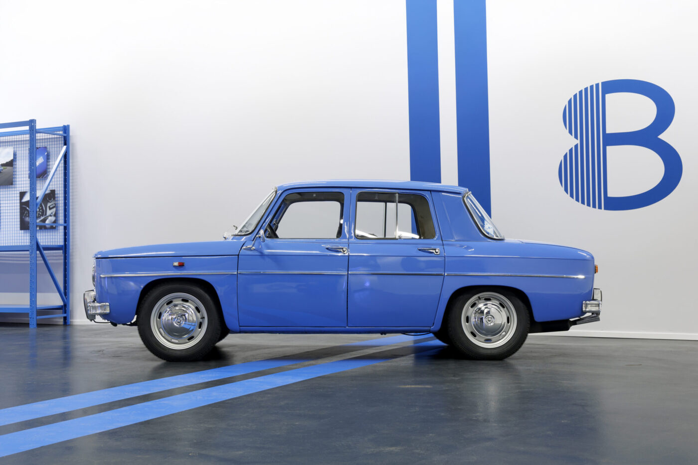Renault 8 Gordini in Blau, Seitenansicht im Studio vor weißer Wand mit blauem „8"-Logo