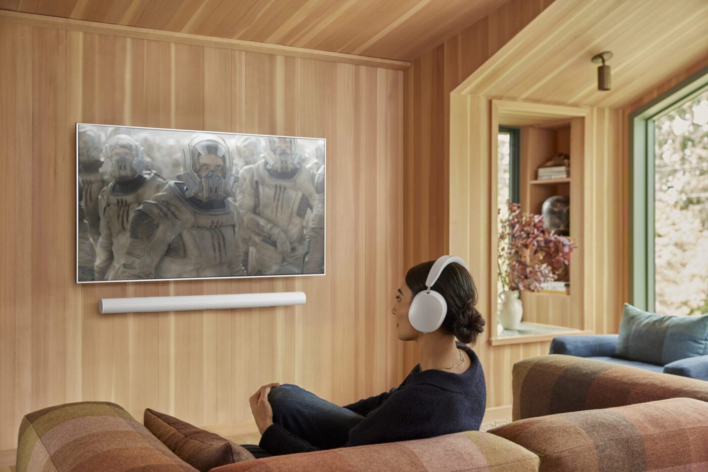 Frau mit weißen Kopfhörern schaut auf wandmontierten TV mit Sonos Soundbar in modernem Wohnzimmer