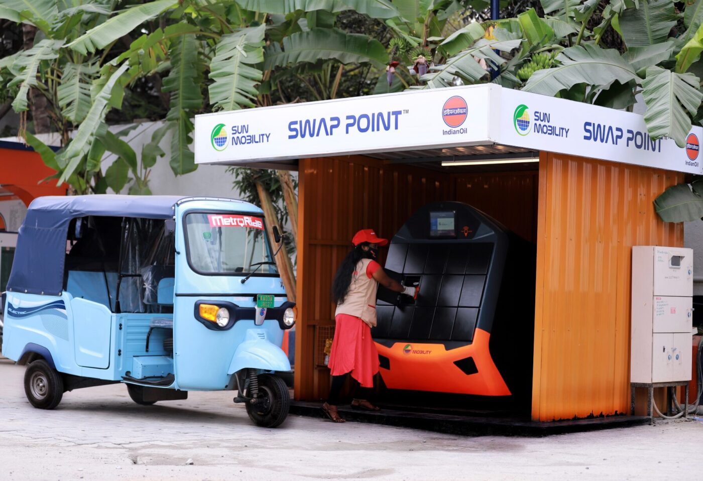 SUN Mobility Swap Point Batteriewechselstation mit Elektro-Tuk-Tuks und Mitarbeiterin an der Wechselmaschine