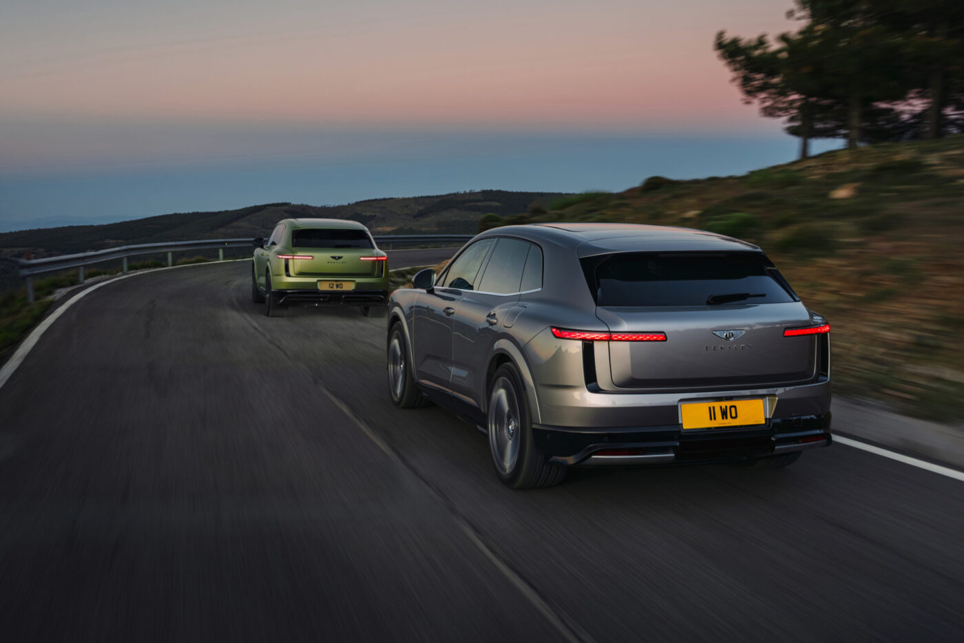 Zwei Bentley Torcal Elektro-SUVs in Grau und Grün auf Landstraße bei Abenddämmerung, Heckansicht