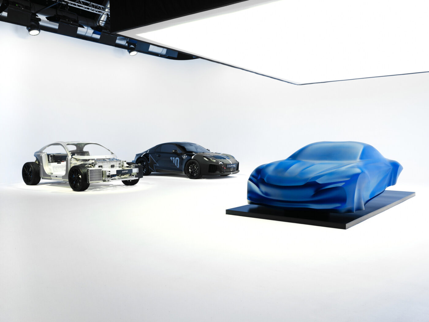 Alpine-Studie der dritten A110-Generation als blau verhüllte Skulptur neben Rennwagen und Antriebsstrang