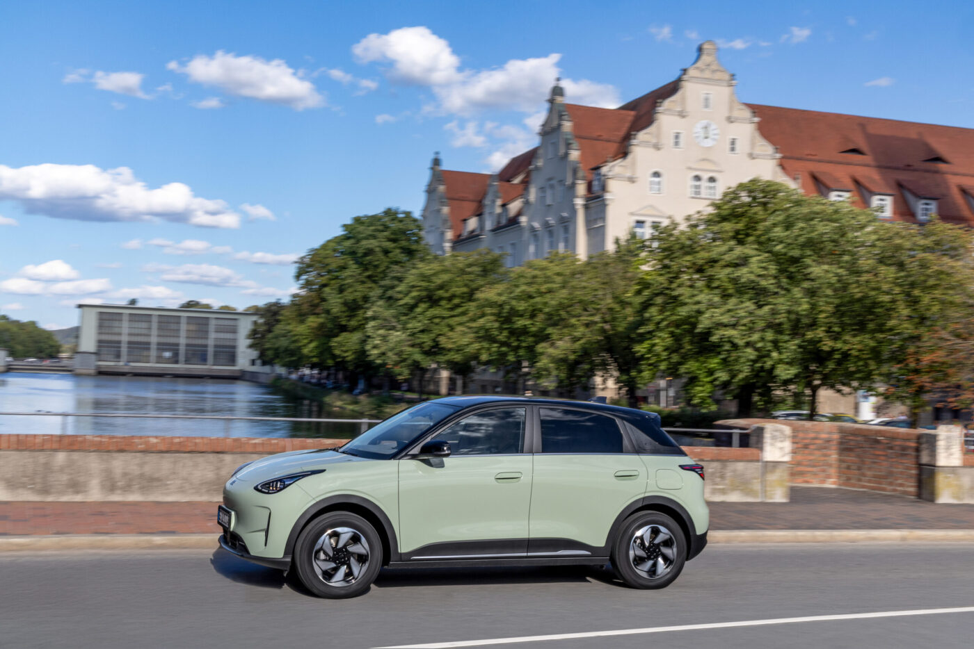 Geely E2 in Hellgrün fährt auf einer Stadtstraße vor historischer Gebäudekulisse