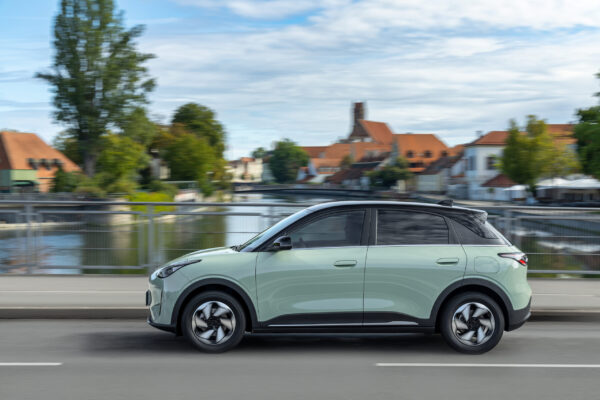 Geely E2 in Mintgrün fährt auf einer Brücke, Seitenansicht, europäische Altstadt im Hintergrund