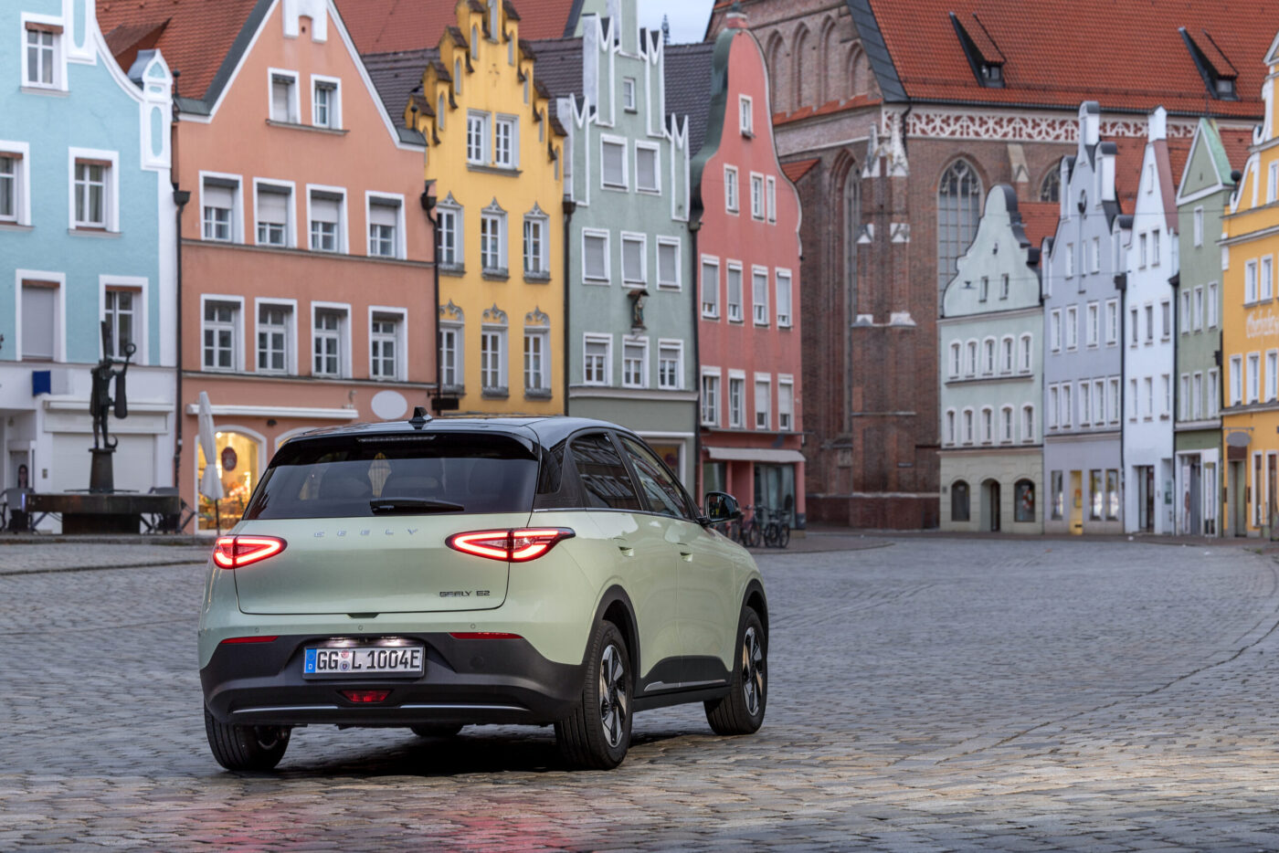 Geely E2 in Mintgrün von hinten auf einem deutschen Altstadtmarktplatz mit bunten Bürgerhäusern