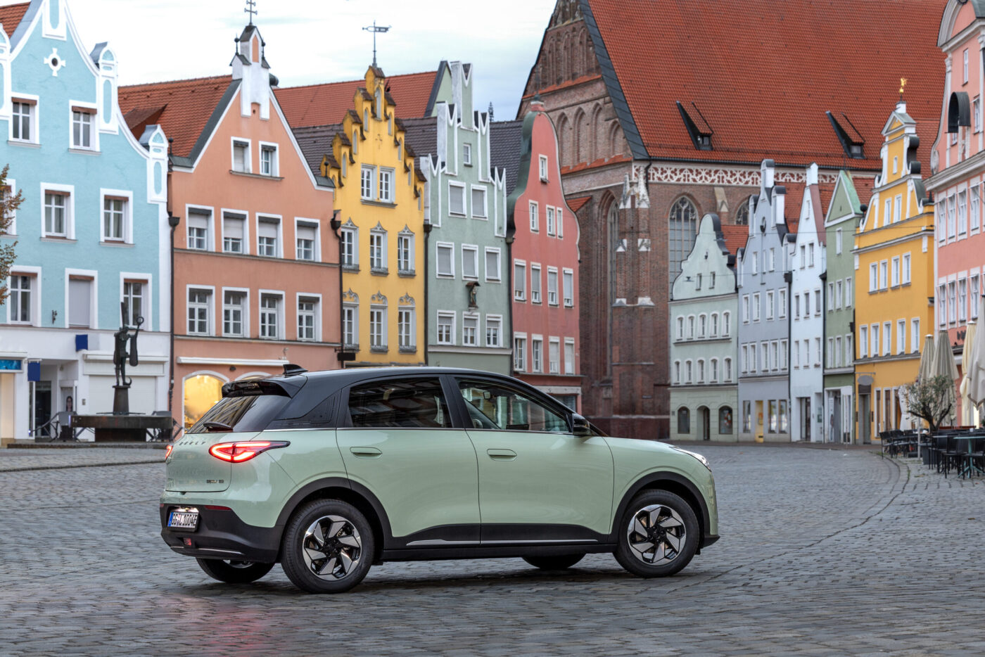 Geely E2 in Hellgrün auf historischem Kopfsteinpflaster-Marktplatz mit bunten Giebelhäusern
